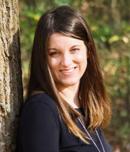 picture of a woman with brown hair smiling by a tree